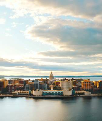 A wide shot downtown Madison surrounded by two lakes, one in the foreground and one in the background. The Wisconsin State Capitol is in the center.