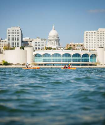 A wide shot of a family kayaking on lake Monona in front of Monona Terrace with the Madison skyline in the background