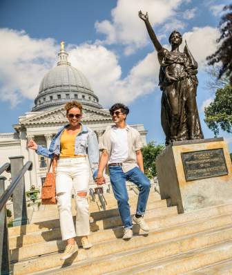 A woman runs ahead of two people holding hands as they walk down the Capitol steps next to the Forward statue/