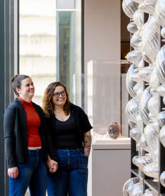 A couple holding hands looking at a glass art piece at the Chazen Museum of Art