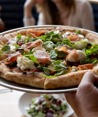 A server about to set down a pizza on the table at Bar Corallini