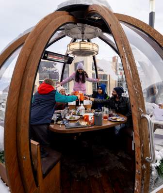 Friends enjoying drinks and dining in an outdoor winter dome at Cafe Hollander in Madison, with snow surrounding the dome.