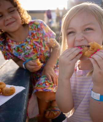 Two young girls eating miniature donuts at a pumpkin patch