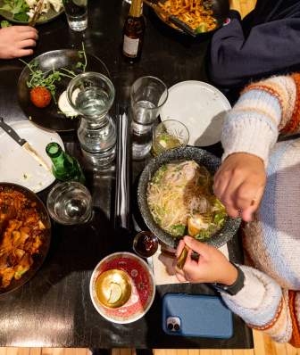 Aerial view of a dining table with various dishes, drinks, and people enjoying a meal together, creating a vibrant culinary experience.