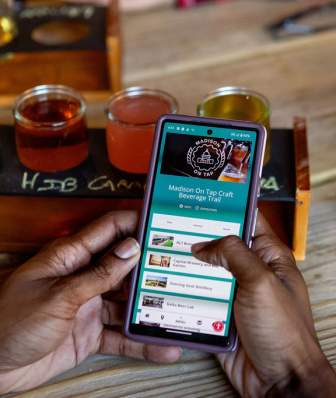 An black man holds a phone at a cidery.