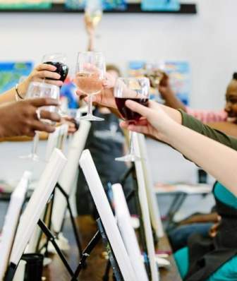 A group of women clinking wine glasses over canvases at a wine and paint event