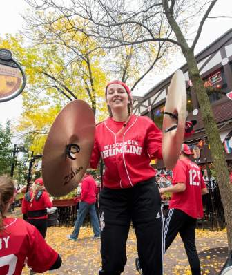 A white woman from the UW Marching Band holds cymbals on a Fall day outside of State Street Brats