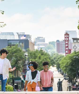 A group of one man and three women walk up the Capitol steps with State Street in the background