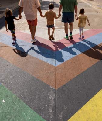 Two men and three young children walk along the rainbow LGBTQ+ pride crosswalk in downtown Madison