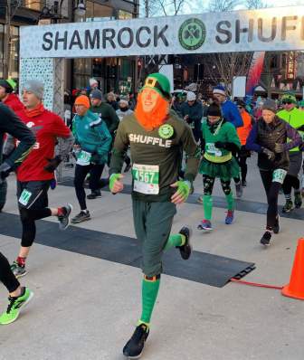 A man wearing a fake red beard and leprechaun hat crosses the finish like at the Shamrock Shuffle run