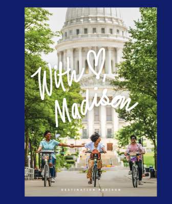 An image of the cover of the Madison Inspiration Guide. The cover has three people riding a bike down State Street while holding hands with the Capitol in the background on it. On top are words that say "With Love, Madison"