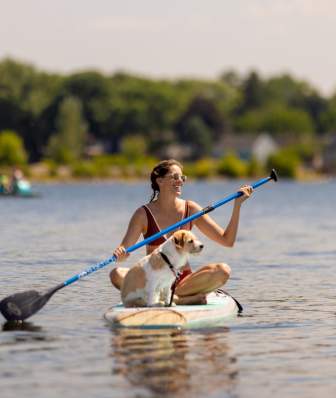 A white woman sits on a paddleboard on the lake with her dog