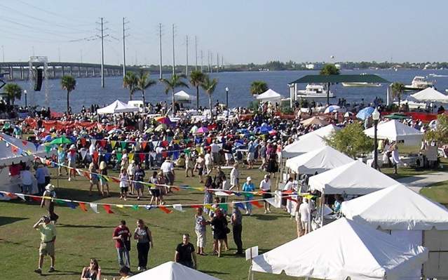 Aerial view of the Wine & Jazz Fest in Punta Gorda: people, vendor tents, the stage, and the Punta Gorda bridges in the background