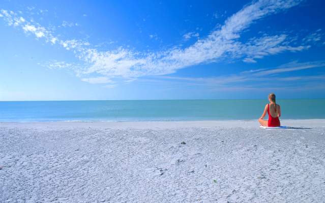 Woman sitting cross-legged near blue water on a clean empty beach