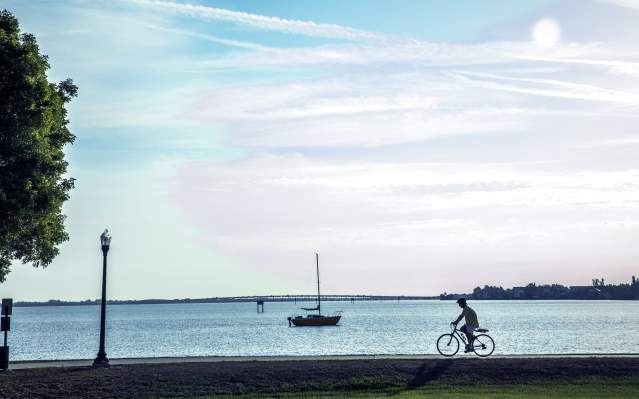 Cyclist on trail next to sailboat on the water