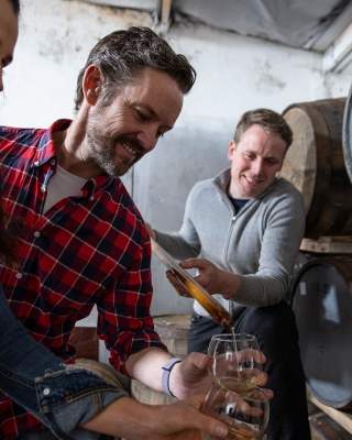 Couple enjoying a tour at Killowen Distillery while the guide pours liquid into their glasses for sampling