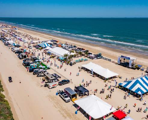 Aerial shot of a long stretch of beach covered in tents and people during a festival.