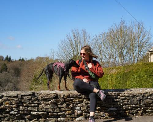 Lottie Gross with her dog sat on a Cotswold stone wall