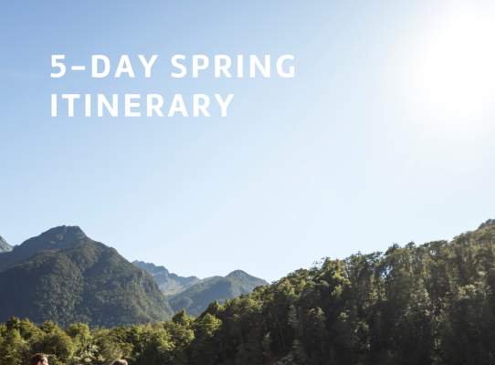 Front cover of a trade itinerary that says '5-day spring itinerary' with three people hiking into the Routeburn with green mountains in the background