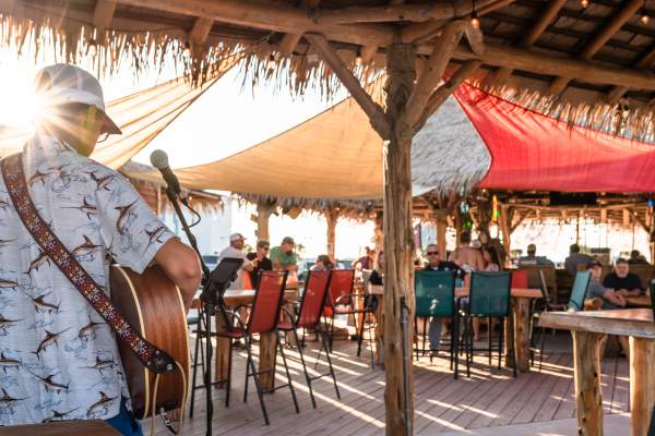 Photo from behind a musician playing guitar towards a tiki bar