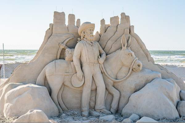 Sand sculpture depicting a prospector holding the reins of a mule in front of some rocks.