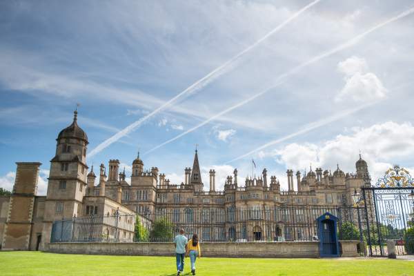 A sunny day exterior of Burghley House near Stamford with two people walking towards the gates