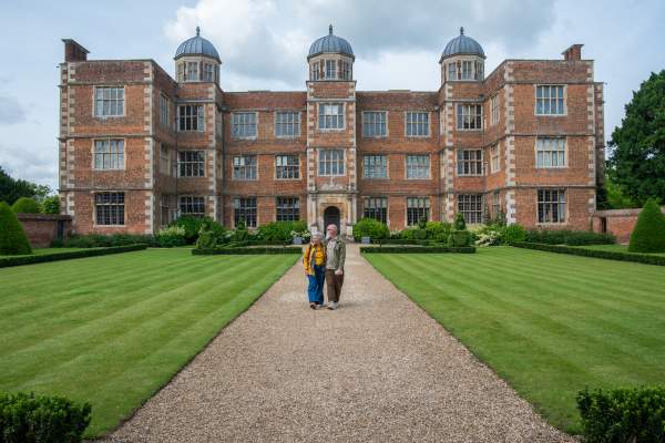 A couple walking in front of Doddington Hall, a heritage house with gardens.