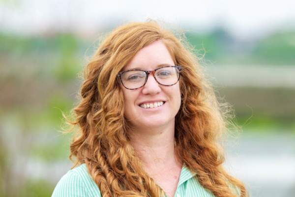 Ashley Bennis smiles at the camera for a headshot. She is wearing a mint green shirt and is in front of an outdoor background.