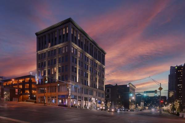 The illuminated Hotel BLU, a historic downtown building, stands on a city street corner beneath a vibrant pink and purple sunset sky.