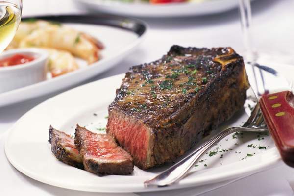 Steak cut open on a plate, medium rare with glass of wine and more plates and glasses blurred in the background.