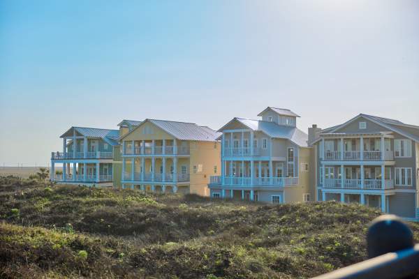 row of 4 large beach houses nestled in dunes in bright sunlight