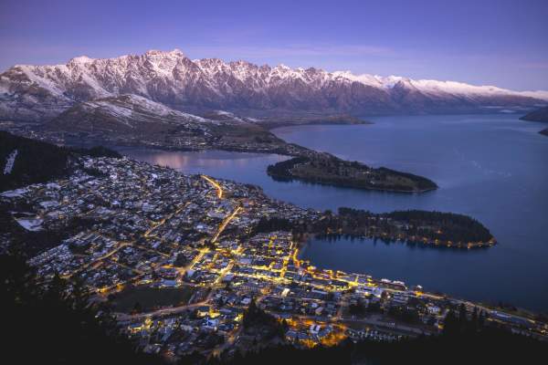 Aerial shot of Queenstown on a winters evening with town street lights glowing and snow capped mountains in the background