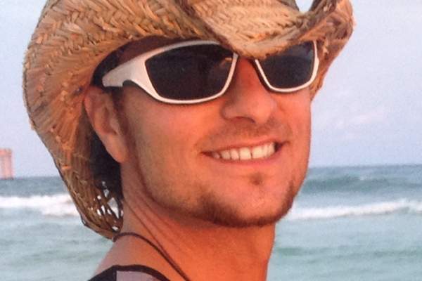 A man in a straw hat smiles at the camera over his shoulder.