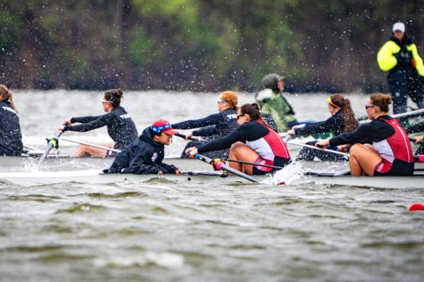 competitive rowing on Ford Lake. Women's team paddling across lake as coaches encourage rowing.