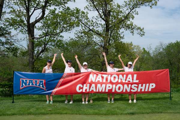 Group of women's golfers in front of NAIA National Championship banner