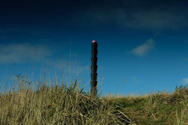 A black active beacon photopost sat within a grassed area with blue skies above.