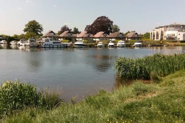 A view of Chertsey Marina over the water of the river Thames. Small boats are moored to the far bank.