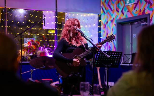 A woman playing an acoustic guitar on a small stage