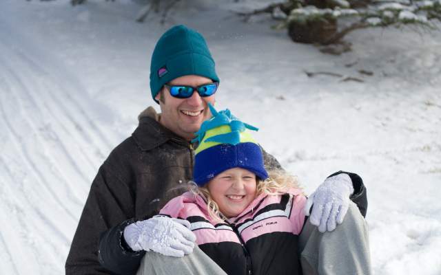 a man and a child ride a sled down a snow covered hill