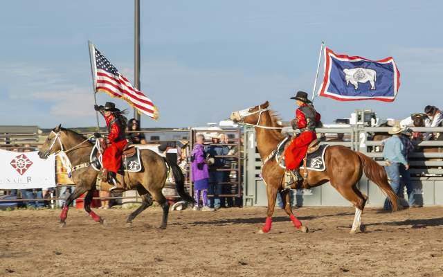 Two horse back riders post the colors at a rodeo
