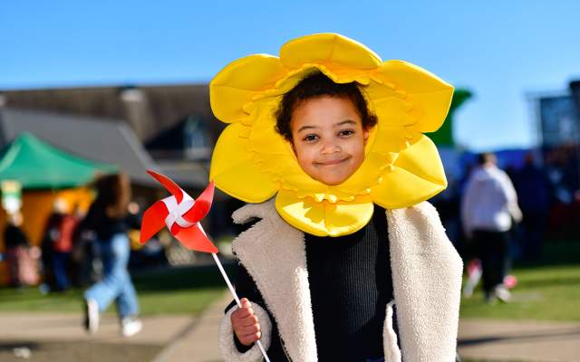 A child wearing a daffodil head dress, holding a windmill.