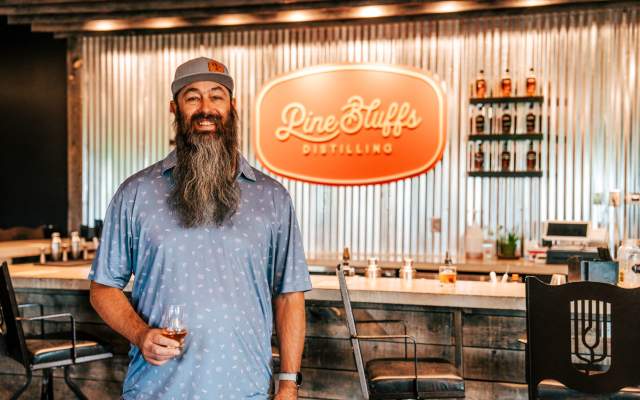 Chad Brown at Pine Bluffs Distilling in Cheyenne, Wyoming, holding a glass of whiskey in front of the distillery's bar.