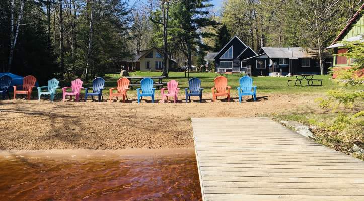 Colorful adirondack chairs on a beach in front of a cottage