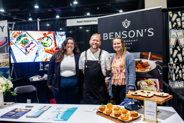 woman, man, and another woman smiling at a booth displaying lobster rolls and smores pie