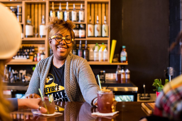 A bartender serving a non-alcoholic cocktail to two bar patrons.