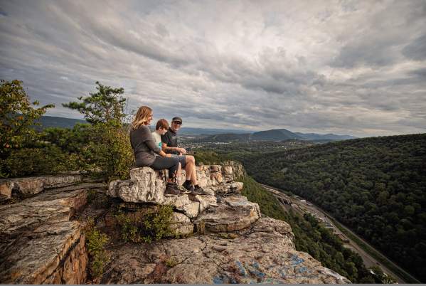 A mom, dad and son sit on a shale cliff overlooking a mountain vista.