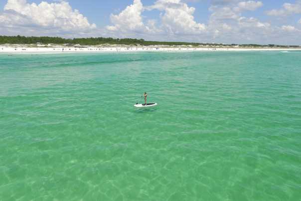 A solitary paddle boarder glides atop a calm emerald sea