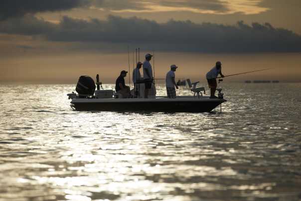 A boat with five anglers are silhouetted by the setting sun.