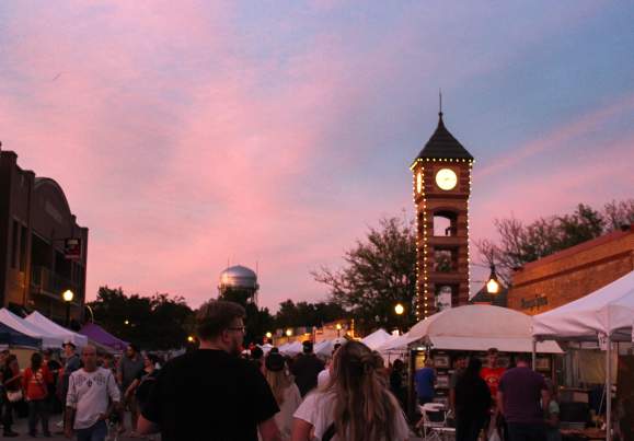 Couple walks through the streets of Downtown Overland Park as a blue, purple and pink sunset is cast over the Clock Tower.