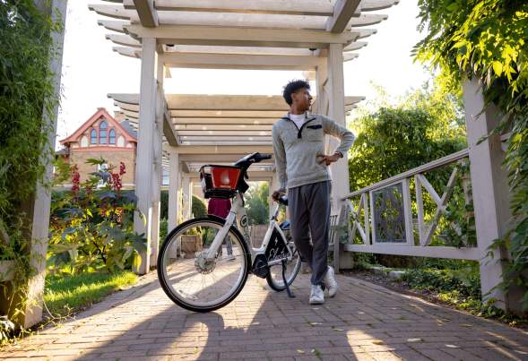 A young Black man stands next to his electric bike while taking in the views at the Allen Centennial Gardens